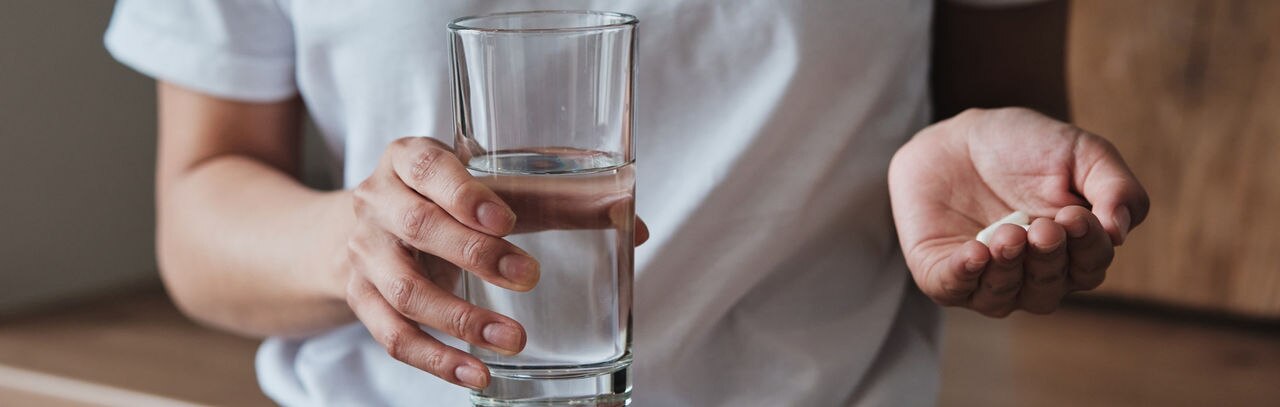 Woman holding pills and glass of water while standing in kitchen at home, cropped photo, people taking vitamins daily, treating disease. Mental health medications, multivitamins and food supplements