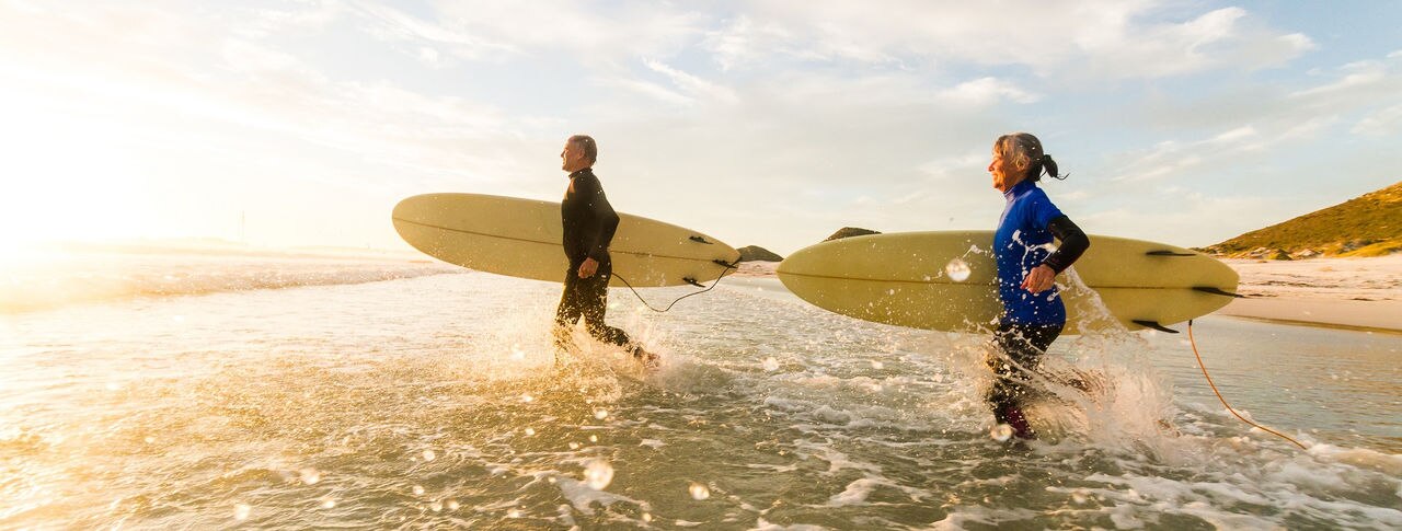 Senior couple (aged65-69) enjoying a surf together in the sea at sunset