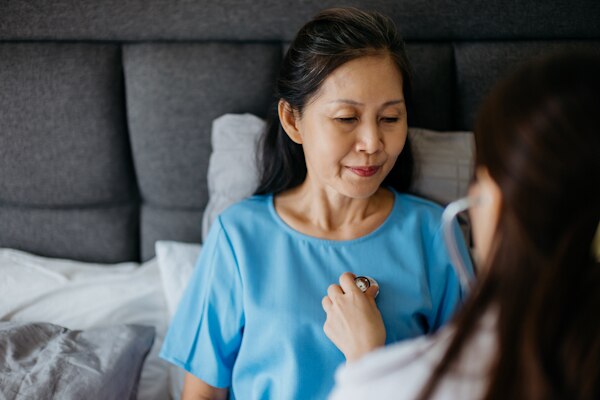 Female doctor using a stethoscope to examining patient's lung and heartbeat during a healthcare home visit
