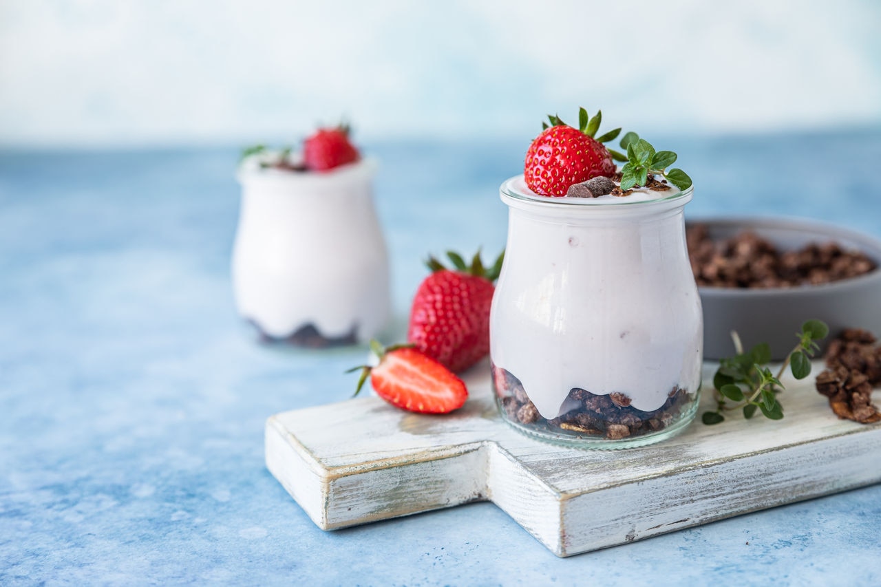 Healthy breakfast or dessert with natural yogurt, chocolate granola and strawberries, blue concrete background.